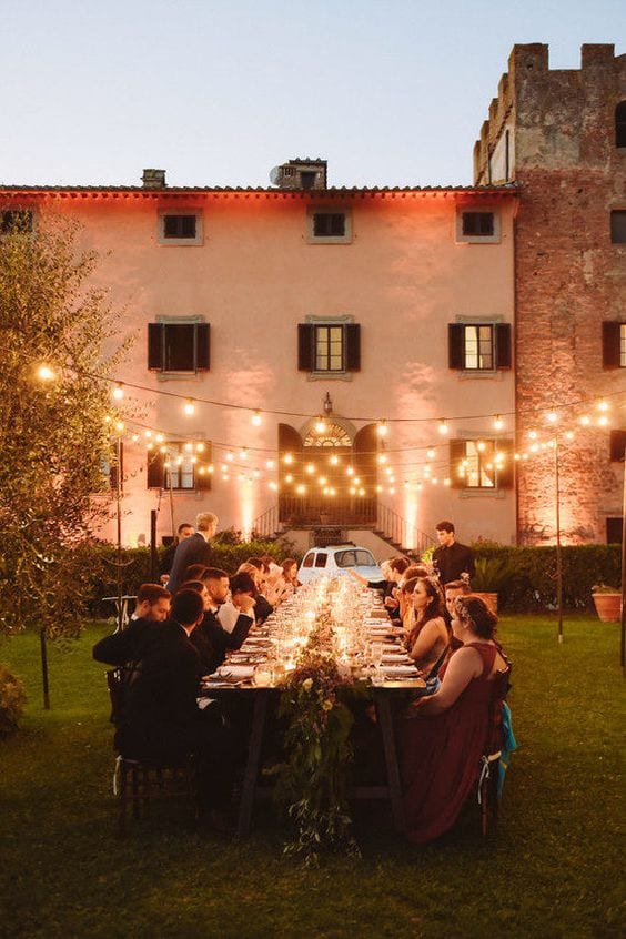Mesa com convidados em volta realizando jantar no campo, e luzes de led iluminando.