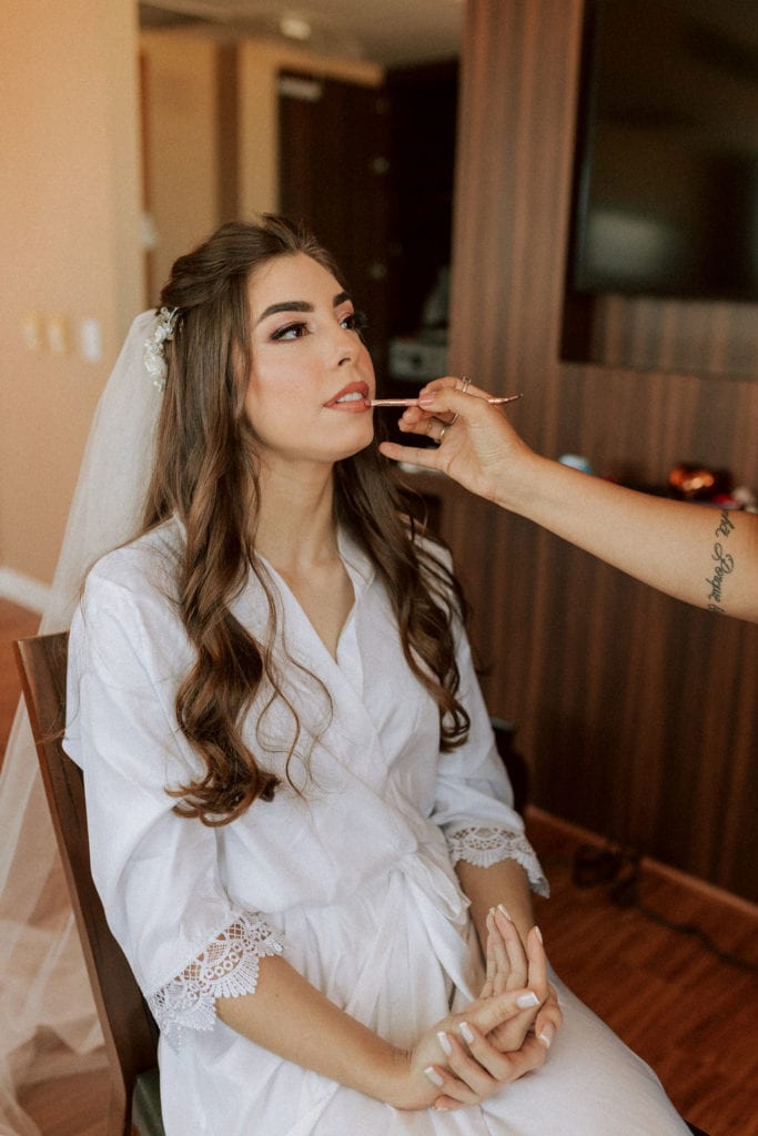 noiva já maquiada retocando o batom, mas ainda de robe