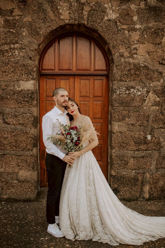noivos posam no alto de um monte de frente para uma capela - fotos pós wedding