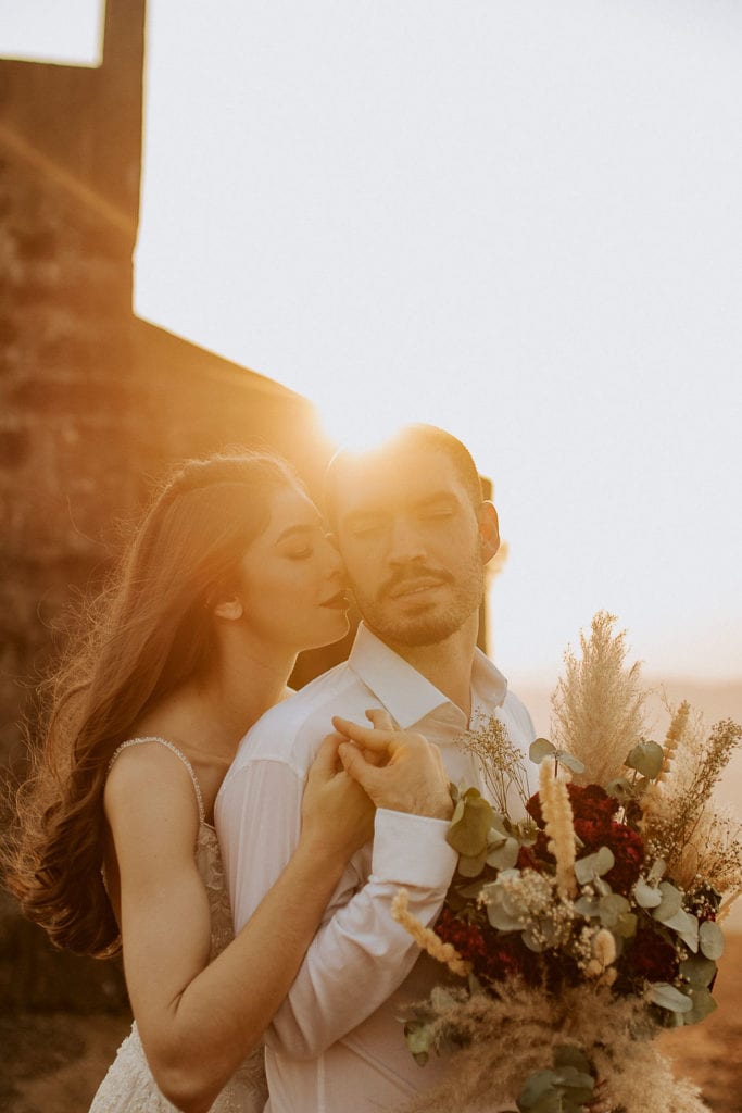noivos posam no alto de um monte de frente para uma capela - fotos pós wedding