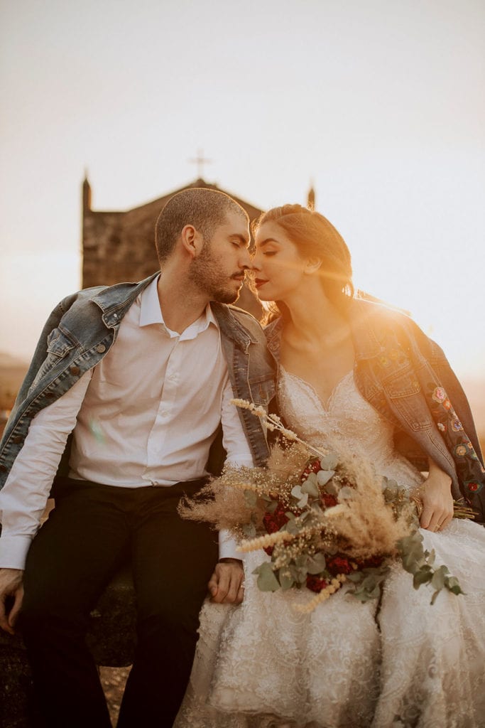 noivos posam no pôr do sol, a noiva usa uma jaqueta e um buquê de folhas secas - fotos pós wedding