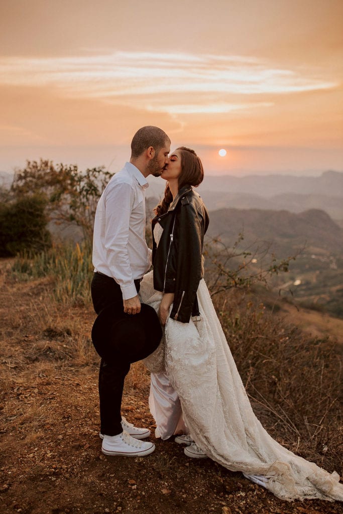 noivos posam no pôr do sol, a noiva usa uma jaqueta e um buquê de folhas secas - fotos pós wedding
